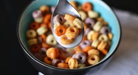 A bowl of cereal loops with some sitting on a spoon.